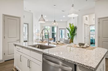 an open kitchen and living room with white cabinets and a granite counter top